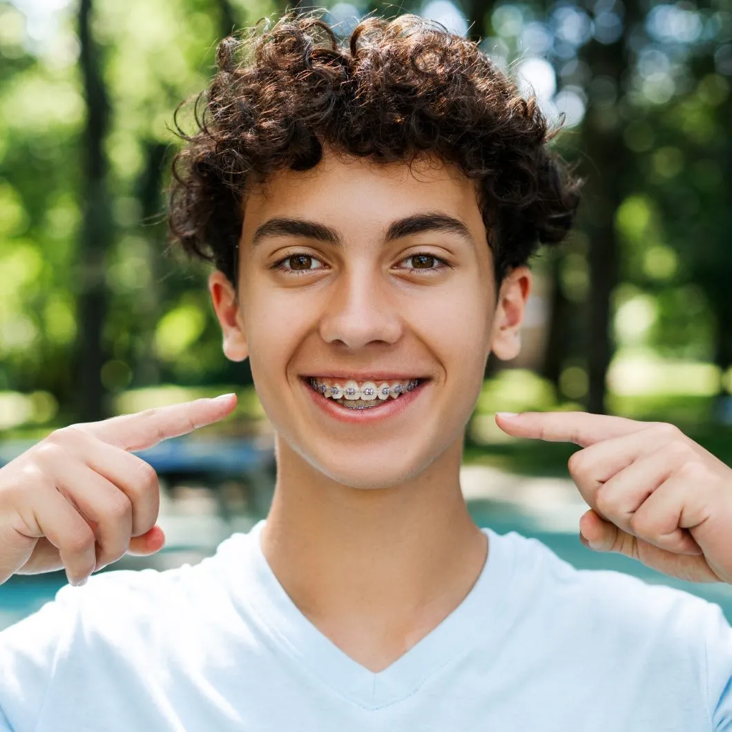 Smiling teenager with curly hair showing self-ligating braces, emphasizing orthodontic treatment benefits in a natural outdoor setting.