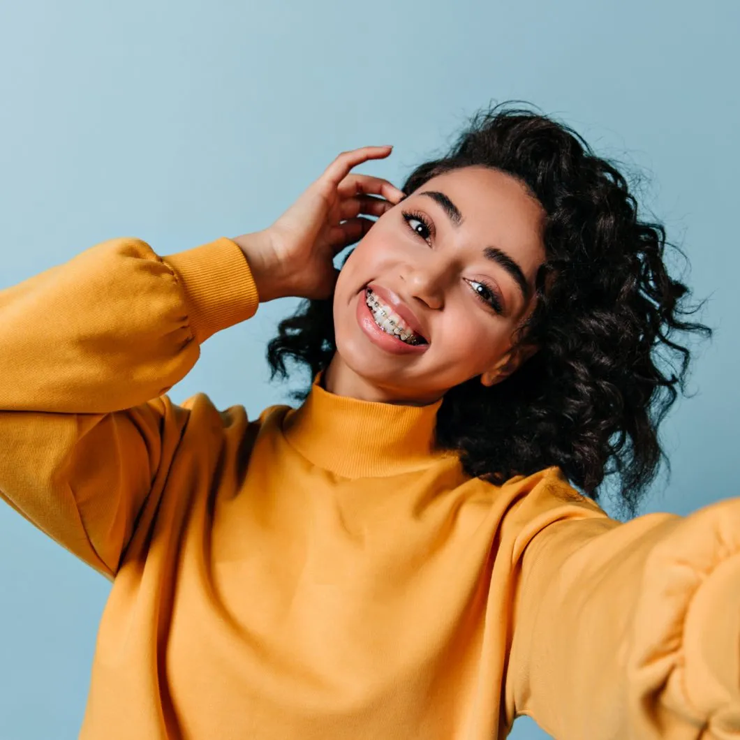 Smiling young woman with braces wearing a yellow sweater, promoting orthodontic care for improved sleep quality.